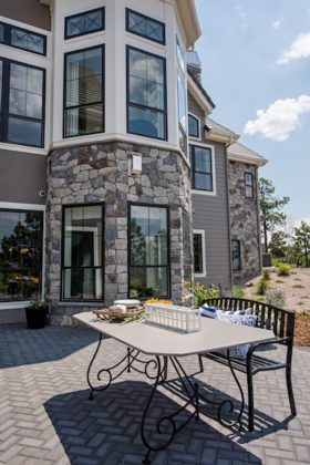 Patio with a gray table, a bench, and view of the stone and gray side of the house in the background