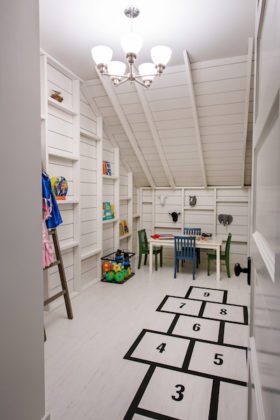 Bright white room with built-in white bookshelves, a hopscotch outlined in black on the floor, and brightly colored children's furniture and toys