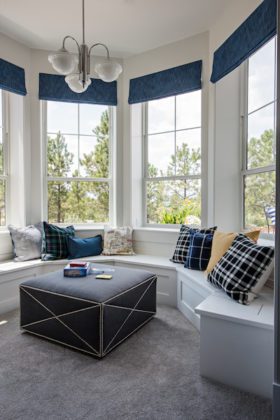 Three tall windows with a long white window seat and cushions