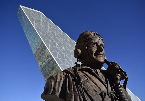 View of a silver geometric building with statue of a man in the foreground
