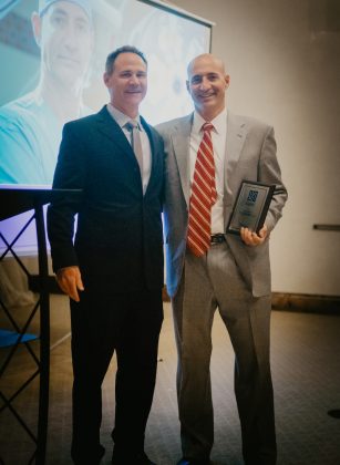 Two men standing and facing the camera, one holding a framed award
