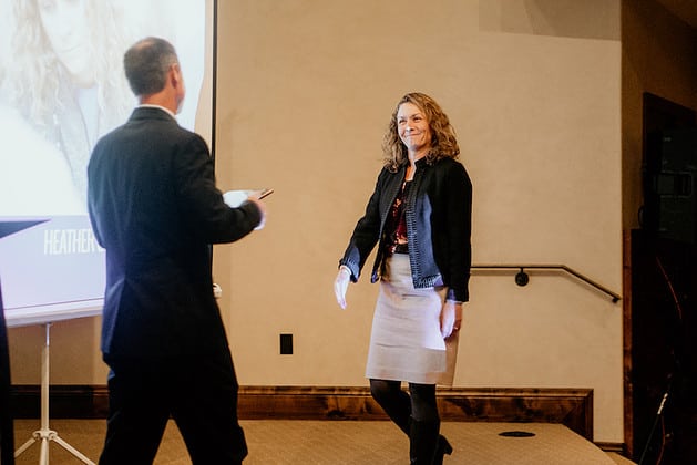Woman walking to accept a framed award from a man holding it towards her