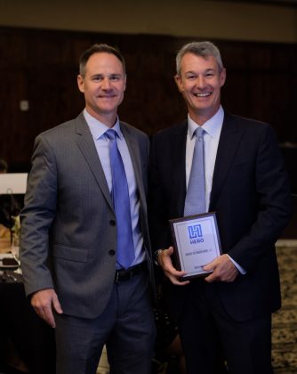 Photo of two men facing the camera, one holding a framed award