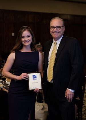 Photo of a woman and a man facing the camera, the woman holding a framed award
