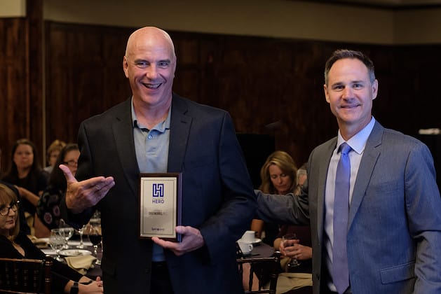 Photo of two men facing the camera, the man on the left holding a framed award
