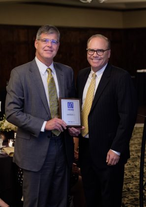 Photo of two men facing the camera, one holding a framed award between them