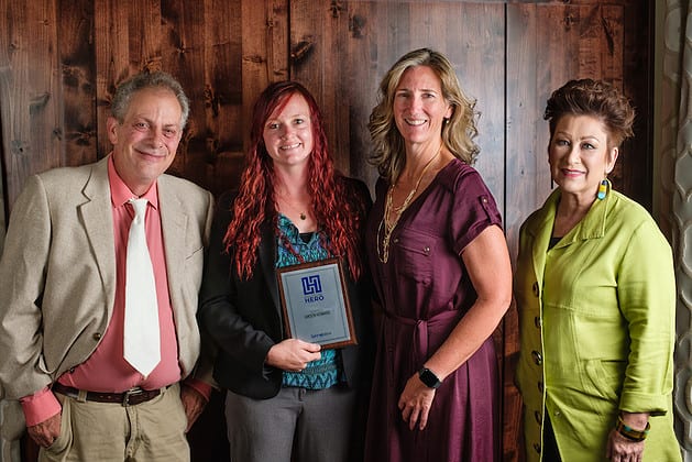 A man and two women facing the camera, the woman in the middle holding a framed award