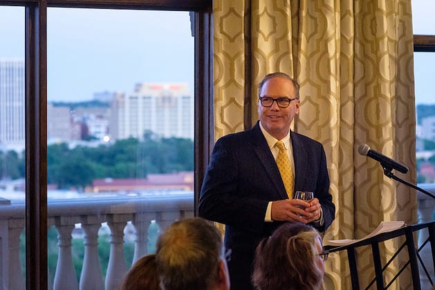 A man holding a drink and looking into the room where other people are seated
