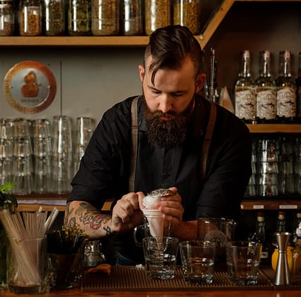 A hip bartender prepares a craft cocktail at Axe and the Oak Whiskey House in Ivywild School, Colorado Springs
