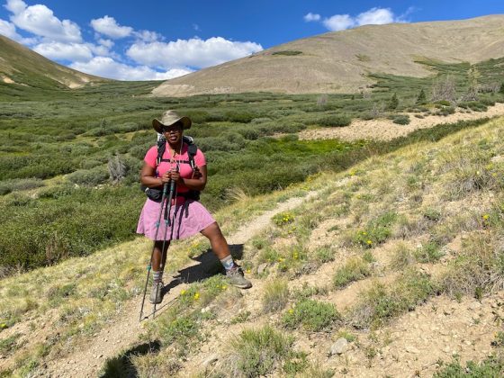 Patricia Cameron standing on a grassy patch with a vast valley of greenery behind her