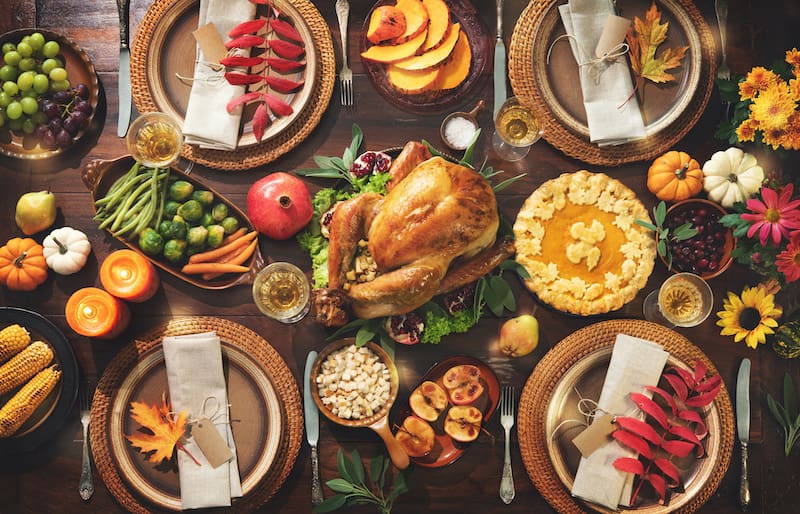 Thanksgiving celebration traditional dinner. Roasted turkey garnished with cranberries on a rustic style table decoraded with pumpkins, vegetables, pie, flowers and candles. Festive table setting