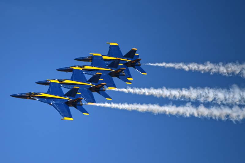 Four U.S. Navy Blue Angels jets flying in formation with smoke trailing. The Blue Angels will perform at the Pikes Peak Regional Airshow in Colorado Springs.