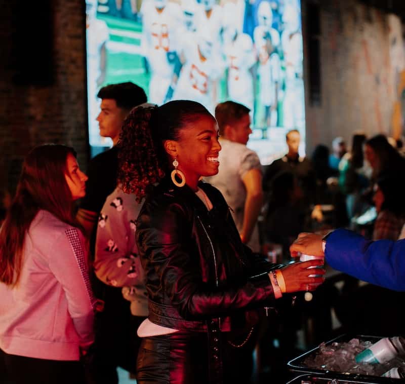 Woman gets a drink at Trainwreck Colorado Springs with big screen in the background. 