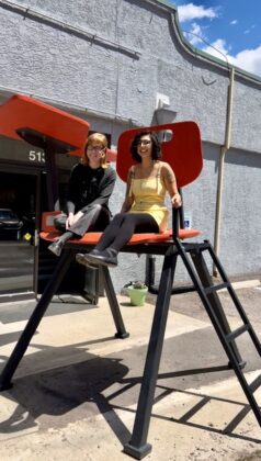 Natalie Johnson and Jasmine Dillavou sit in the giant red chair outside the Manitou Art Center