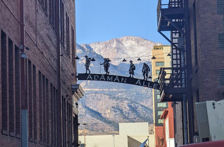 Bronze climbers on title archway of AdAmAn Alley with Pikes Peak in the background.