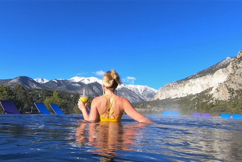 Woman with a drink enjoys the view from Mt Princeton hot springs resort infinity pool