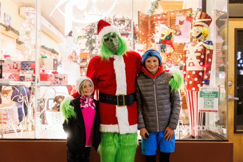 Grinch stands in front of store window with two children during holiday shopping in Colorado Springs.