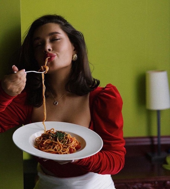 A woman in a red dress closes her eyes and savors a pasta dish at Evergreen, one of the most romantic restaurants for date night in Colorado Springs. 