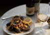 A plate of seafood pasta, Mussels with Nduja & White Wine, and a glass and bottle of white wine at Oro, one of the best restaurants in Colorado Springs.