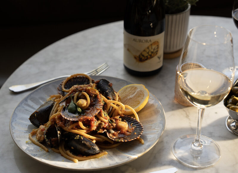 A plate of seafood pasta, Mussels with Nduja & White Wine, and a glass and bottle of white wine at Oro, one of the best restaurants in Colorado Springs.