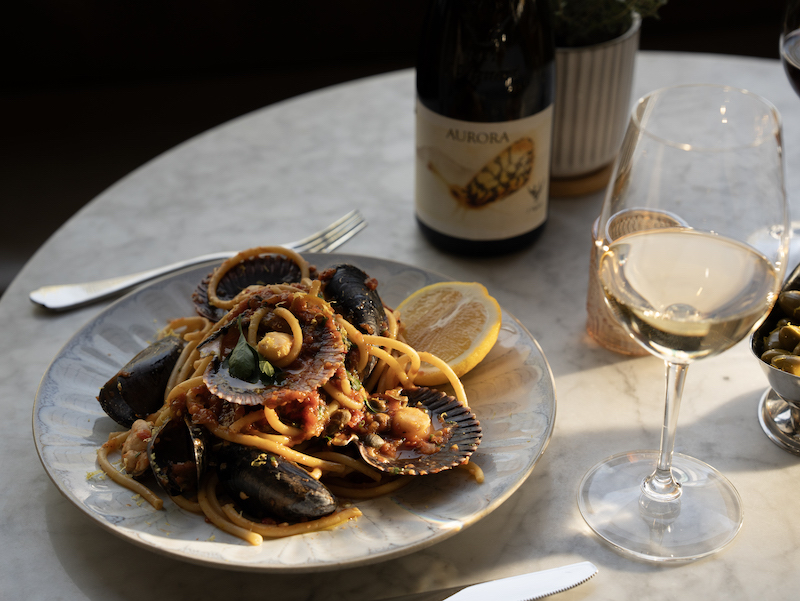 A plate of seafood pasta, Mussels with Nduja & White Wine, and a glass and bottle of white wine at Oro, one of the best restaurants in Colorado Springs.