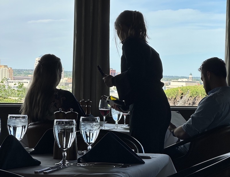 A waitress pours wine for a couple silhouetted against the views of the downtown Colorado Springs skyline at The Peppertree restaurant.