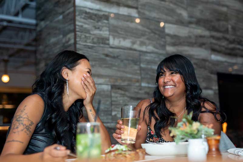 Two women laugh over a meal at Till Neighborhood Bistro & Bar, one of the best restaurants in Colorado Springs.