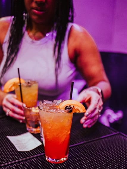 woman reaching for her two drinks from the bar at Luchal's.