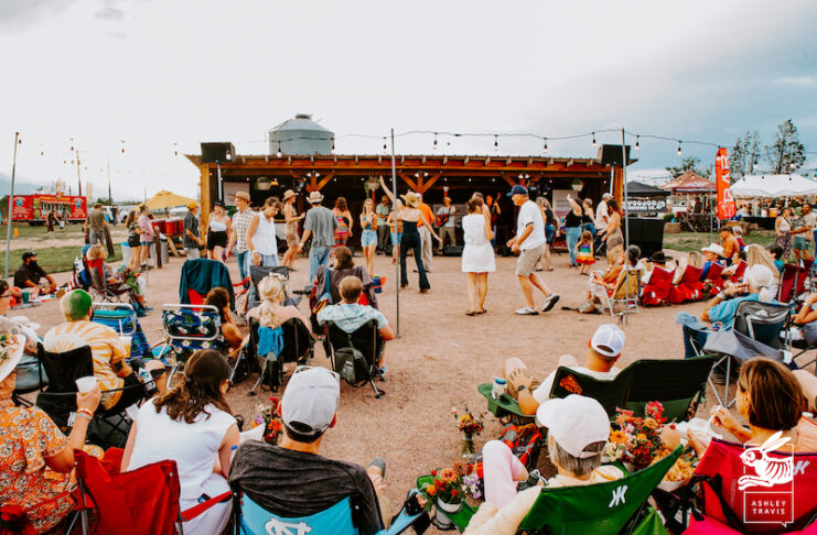 The band plays. Dancers dance in the barnyard. People sit in the audience with bouquets of flowers at Rocky Mountain Flower Fest.