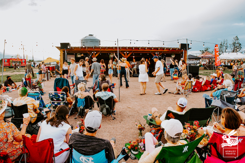 The band plays. Dancers dance in the barnyard. People sit in the audience with bouquets of flowers at Rocky Mountain Flower Fest.