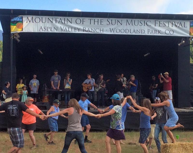 Dancers hold hands in a circle in front of the stage at Mountain of the Sun Music Festival at Aspen Valley Ranch in Woodland Park, Colorado.