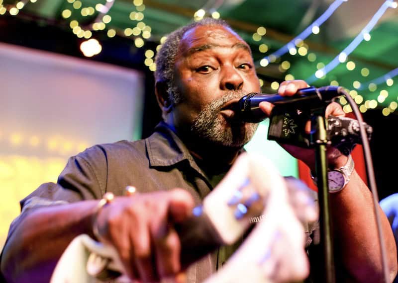 Blues singer Rex Peoples points at the camera while playing the blues.