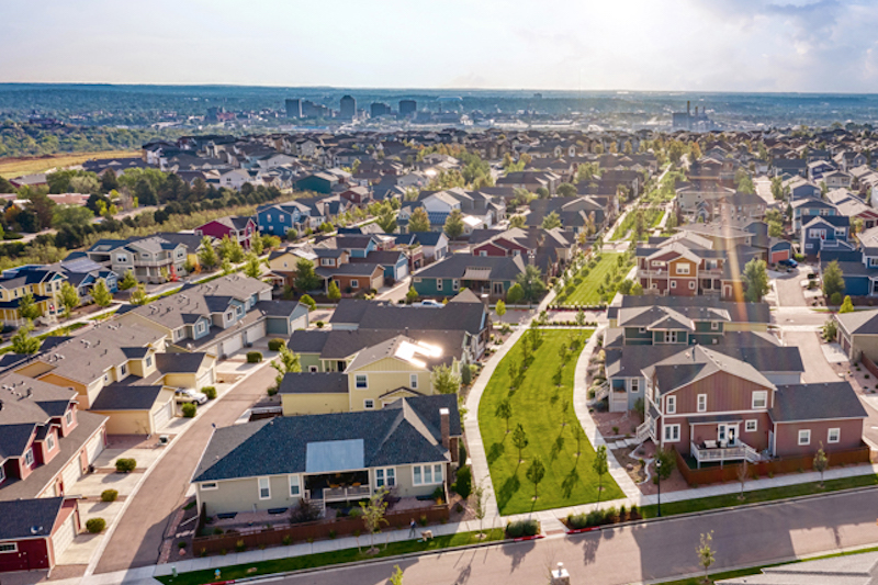 Aerial view of the streets and greenspaces of the planned community Gold Hill Mesa with the downtown Colorado Springs skyline on the horizon