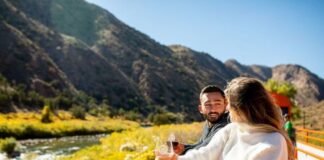 12 Creative Ways to Experience Colorado Fall Colors A man and woman hold wine glasses on open car of Royal Gorge Railroad, passing by Colorado fall colors