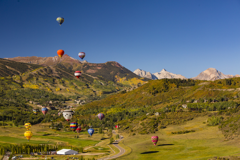 Hot air balloons rise above golden hillsides surrounding Snowmass at the Snowmass Balloon Festival