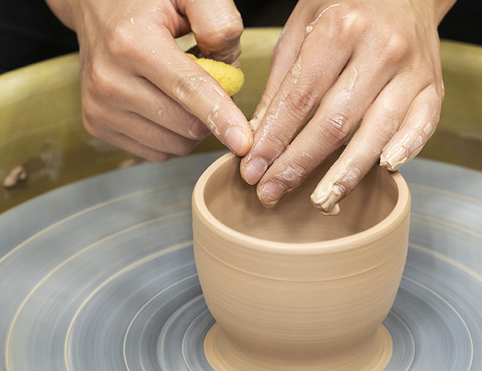 Hands shaping a clay pot on a pottery wheel at Bemis Art School.