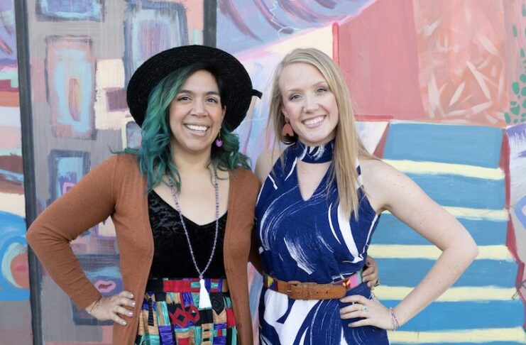 two women stand in front of colorful mural in vintage clothing.
