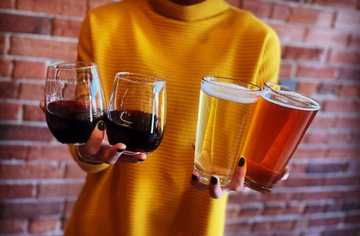 Woman holding two beers and two glasses of wine at Odyssey Gastropub, one of the best spots for happy hour in Colorado Springs