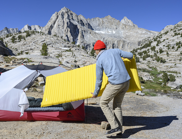 A camper puts a Therm-A-Rest Neo Air sleeping pad into a tent with the Sierra mountains in the background