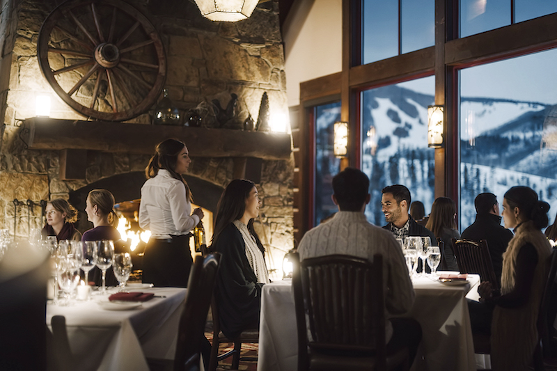Couples dine inside Allie's Cabin at Beaver Creek beside a stone fireplace and views of the ski slopes at Beaver Creek resort.