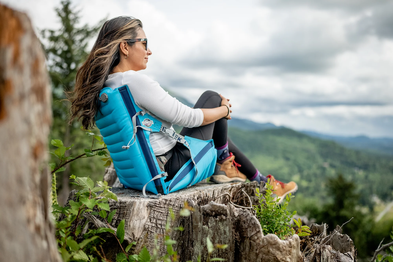 A woman sits in a Crazy Creek AirCliner on a mountainside.