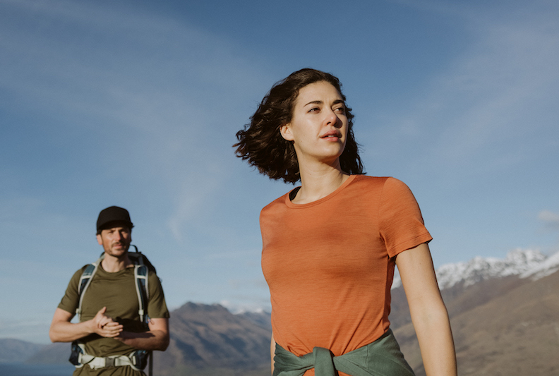 A woman and man hike in the mountains wearing Icebreaker Tech-Lite T-shirts