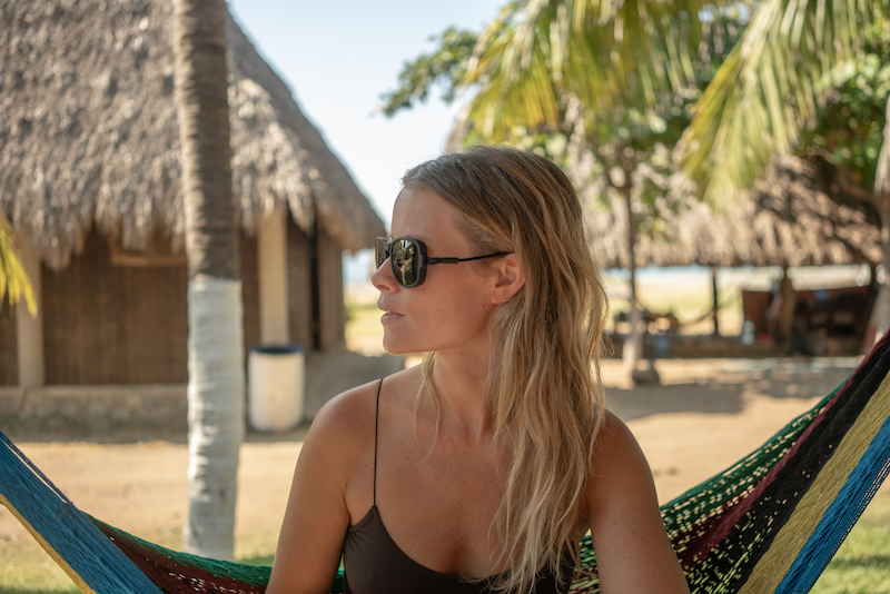 A woman wears Ombraz sunglasses in a beach hammock.
