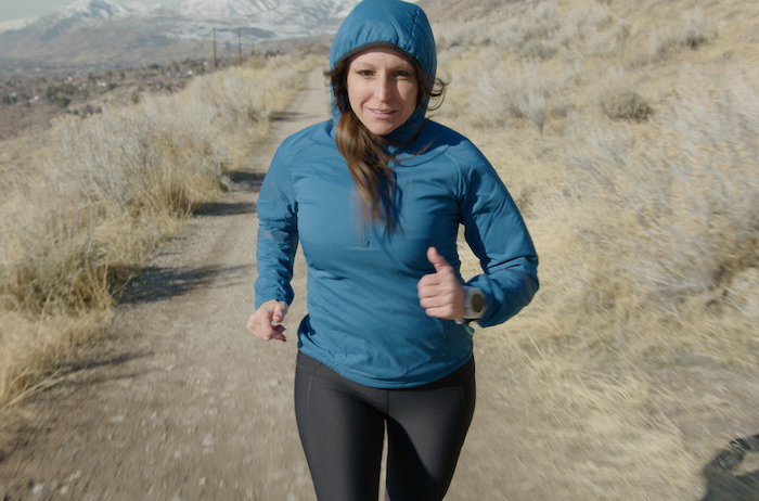 A woman runs on a trail wearing a blue Outdoor Vitals Ventus hoodie
