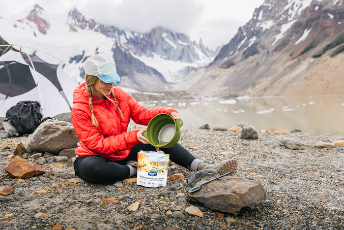 A woman cooks a Backpacker's Pantry freeze dried meal with epic Patagonia mountains behind her