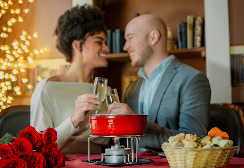 A couple toasts wine glasses over fondue at the Mona Lisa, one of the most romantic restaurants in Colorado Springs. 