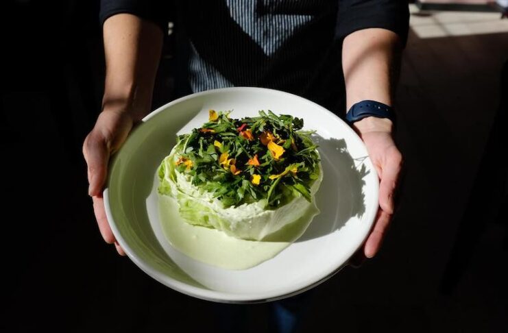 Hands hold an artistic salad from Bin 707 Foodbar, a Colorado James Beard Awards semifinalist 2025