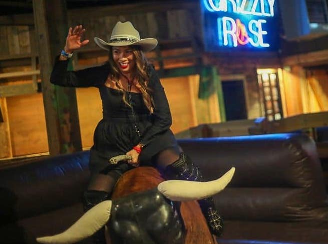A woman in a cowboy hat rides a mechanical bull at the Grizzly Rose. The bar's new Whiskey Rose in Colorado Springs will have one too.