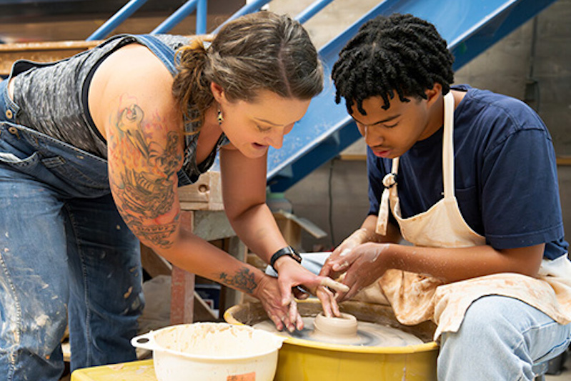 An instructor at student work at the pottery wheel at the Bemis School of Art.