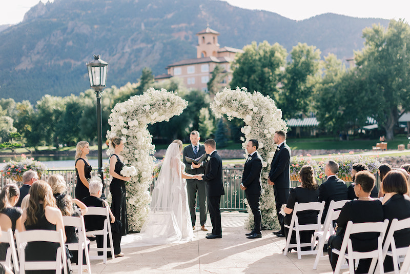 A wedding ceremony on the Lakeside Terrace at the Broadmoor with floral arch and Cheyenne Mountain in the background.